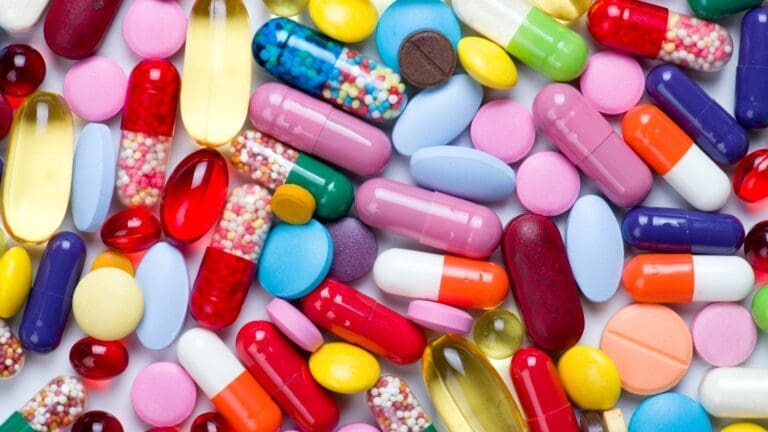 A colorful assortment of various pills, including antibiotics often prescribed before a dental procedure, is scattered on a white surface.