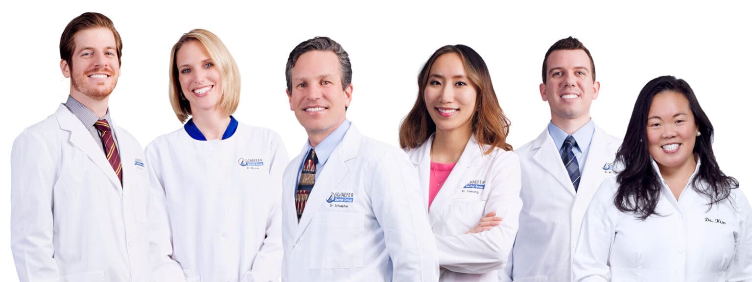 Six medical professionals standing side by side, all wearing white lab coats and smiling, against a plain white background.